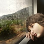 child-staring-out-of-window-at-rain